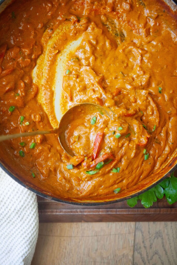 Coconut curry in a pan with ladle.