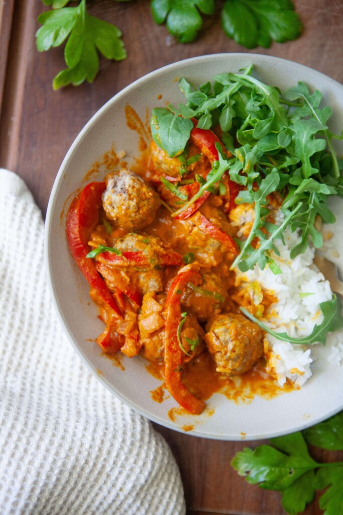 Coconut curry with peppers served with meatballs, rice and arugula in a bowl.