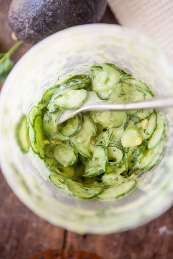 Upclose of creamy cucumber salad mixed together in large plastic container with long spoon.