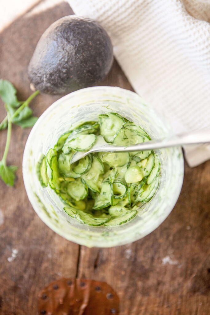 Creamy cucumber salad mixed together in large deli container with spoon.
